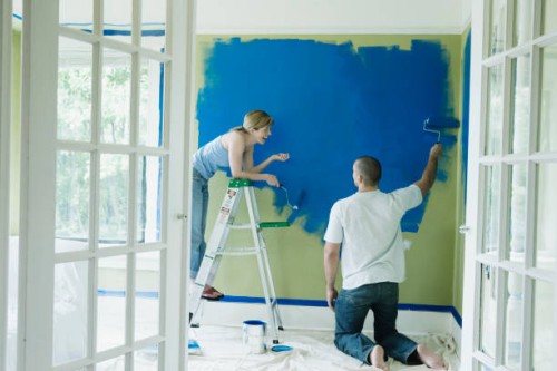 young couple conversing while painting wall - home decoration stock pictures, royalty-free photos & images