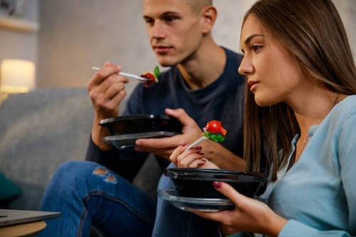 young couple enjoying healthy takeaway lunch and watching a movie on laptop - junk food stock pictures, royalty-free photos & images