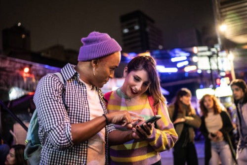 young couple (or friends) using mobile phone at festival by the night - including a transgender person - fashion stock pictures, royalty-free photos & images