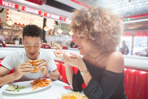 young couple, sitting in diner, eating meal - junk food stock pictures, royalty-free photos & images