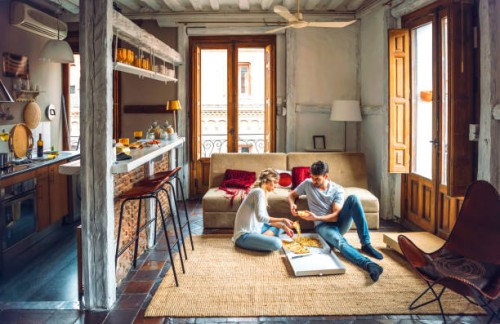 young couple sitting on floor of living room and eating pizza from box - junk food stock pictures, royalty-free photos & images