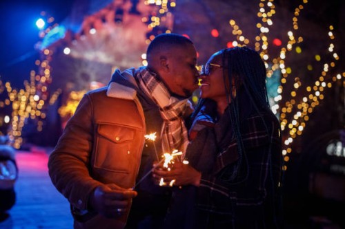 young couple waving sparklers and kissing while celebrating new year's eve on at the concert - concert stock pictures, royalty-free photos & images