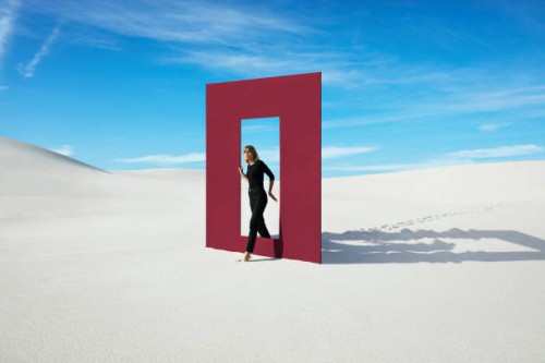 young fashion model walking through red door frame at desert against sky - fashion stock pictures, royalty-free photos & images