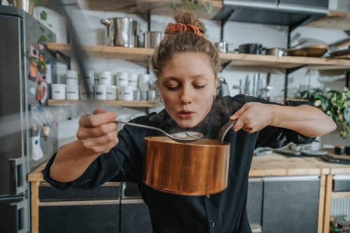 young female chef tasting broth soup while standing in kitchen - food stock pictures, royalty-free photos & images