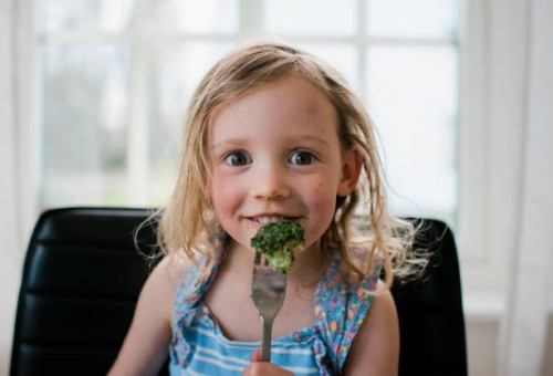 young girl eating broccoli at home with a messy face - food stock pictures, royalty-free photos & images
