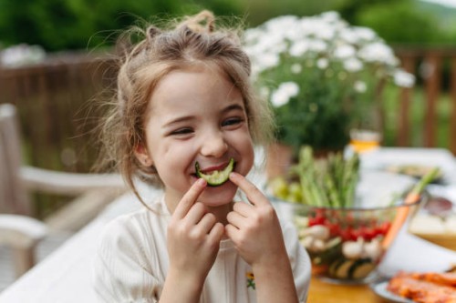 young girl eating slice of cucumber, having fun, waiting for grilled food. family barbecue in backyard, spending quality time outdoors together. - food stock pictures, royalty-free photos & images