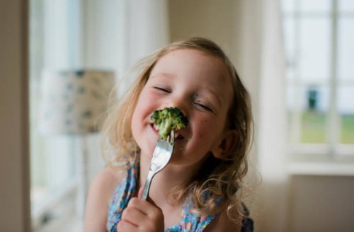 young girl laughing with a messy face whilst eating broccoli - food stock pictures, royalty-free photos & images