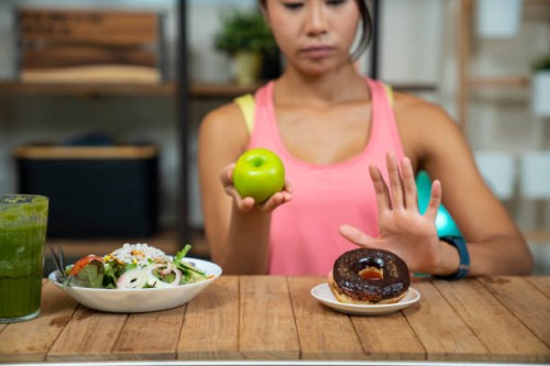 young girl on dieting for good health concept. close up female using hand reject junk food by pushing out her favorite donuts and choose red apple and salad for good health - junk food stock pictures, royalty-free photos & im