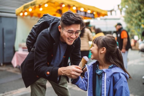 young handsome dad feeding ice cream to her lovely daughter in front of ice cream stall in food market - junk food stock pictures, royalty-free photos & images