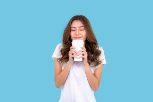 young happy asian woman feeling happiness wearing white shirt standing isolated over cyan background, holding takeaway coffee cup - junk food stock pictures, royalty-free photos & images