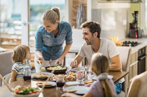 young happy woman serving lunch to her family at dining table. - food stock pictures, royalty-free photos & images