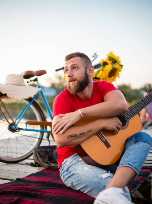 young hipster guy holding acoustic guitar while sitting on dock in nature. summer and travel concept. - concert stock pictures, royalty-free photos & images