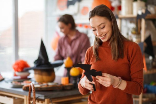 young joyful woman cutting out a paper bat when making halloween decorations - home decoration stock pictures, royalty-free photos & images