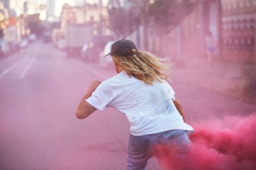 young male skateboarder wearing white t-shirt carrying a pink flare as he skates away down the street - fashion stock pictures, royalty-free photos & images