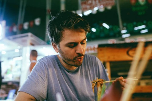 young man eating authentic thai food on a street market in bangkok, thailand - food stock pictures, royalty-free photos & images