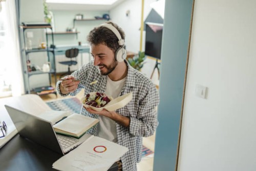 young man eating take away meal and looking at the laptop - junk food stock pictures, royalty-free photos & images