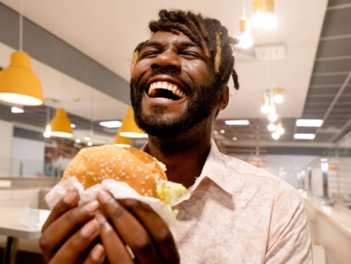 young man enjoying having burger at a restaurant - junk food stock pictures, royalty-free photos & images