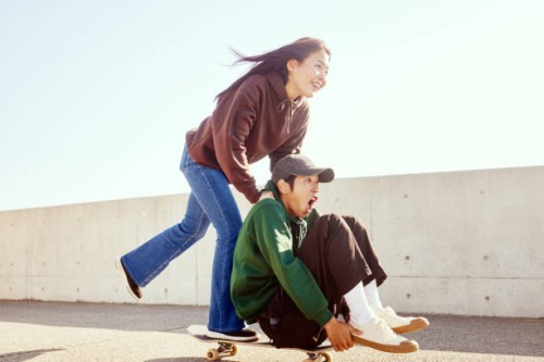 young man enjoys pushing his friend sitting on a skateboard from behind with his hand. - fashion stock pictures, royalty-free photos & images