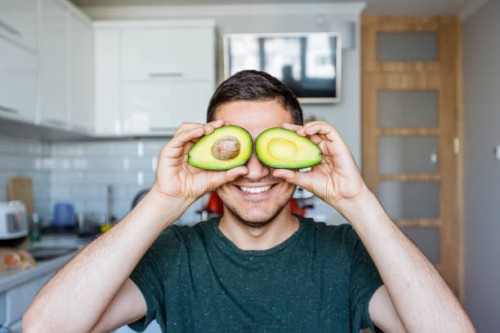 young man having fun with avocado at the kitchen - food stock pictures, royalty-free photos & images