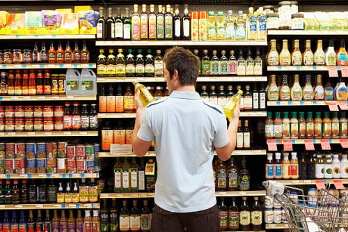 young man in supermarket comparing bottles of oil, rear view, close-up - food stock pictures, royalty-free photos & images