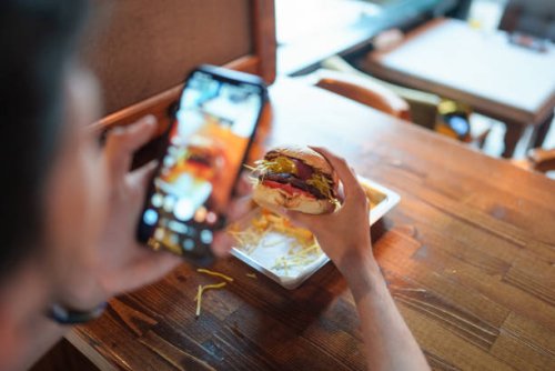 young man is taking a photo of his burger with his phone - food stock pictures, royalty-free photos & images