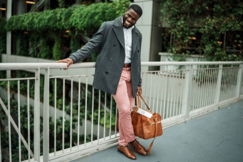 young man laughs, holding duffel bag outside airport - fashion stock pictures, royalty-free photos & images