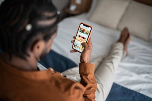young man ordering food online with smartphone at home - food stock pictures, royalty-free photos & images