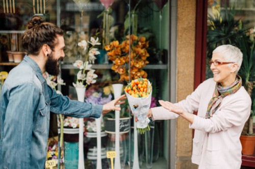 young man taking a flower bouquet from a senior florist - garden decoration stock pictures, royalty-free photos & images