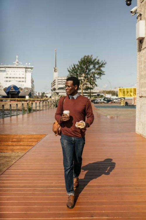 young man with coffee cup and hamburger walking at the harbour - junk food stock pictures, royalty-free photos & images