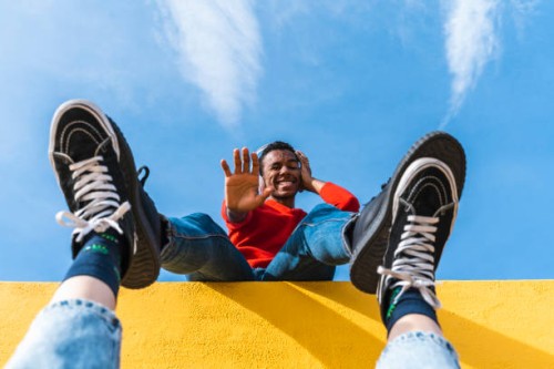 young man with headphones, dancing for person, leaning on yellow wall - fashion stock-fotos und bilder