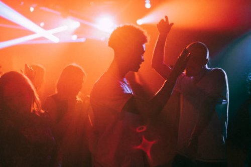 young men and women dancing against illuminated red spotlights at nightclub - concert stock pictures, royalty-free photos & images