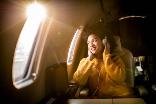 young modern woman sitting in a private jet, listening to music through the headphones and looking through the window - travel stock pictures, royalty-free photos & images