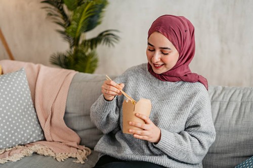 young muslim woman eating take out food on the sofa at home - junk food stock pictures, royalty-free photos & images