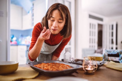 young pretty asian woman tasting a dish of pasta she prepared while serving food on the table at home - food stock pictures, royalty-free photos & images