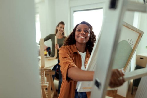 young smiling woman deciding where to put picture in new apartment - home decoration stock pictures, royalty-free photos & images