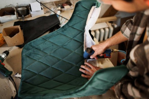 young upholstery worker applying fabric on a chair with a pneumatic stapler in the workshop - home decoration stockfoto's en -beelden