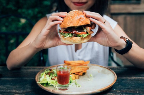 young woman eating burger at restaurant with outdoor seating - junk food stock pictures, royalty-free photos & images