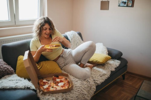 young woman eating pizza in living room - junk food stock pictures, royalty-free photos & images