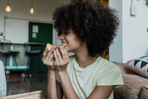young woman eating slice pizza in the living room at home - junk food stock pictures, royalty-free photos & images