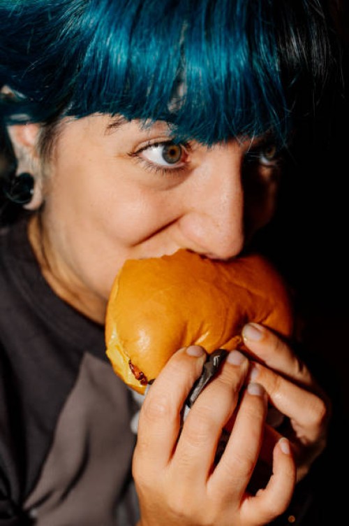 young woman enjoying a delicious burger at home: food delivery - junk food stock pictures, royalty-free photos & images