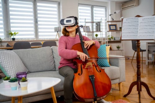 young woman experiencing virtual reality of a sold out concert while playing violoncello at home - concert stockfoto's en -beelden