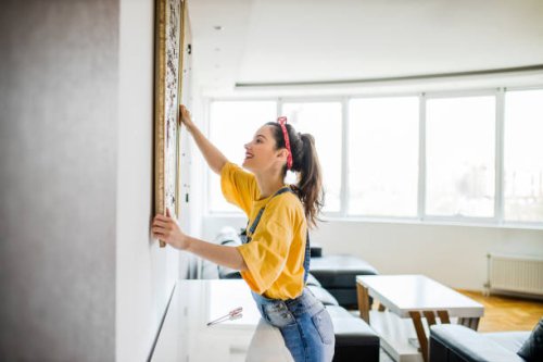 young woman hanging a picture on a wall with a look of concentration - home decoration stock pictures, royalty-free photos & images