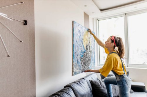 young woman hanging art picture on wall and decorating living room - home decoration stock pictures, royalty-free photos & images