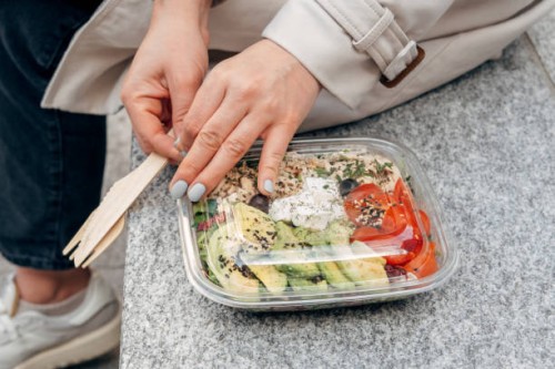young woman holding a large portion of takeaway salad with chicken, avocado tomato and feta cheese, takeaway food , woman eating lunch outside outside the office - junk food stock pictures, royalty-free photos & images