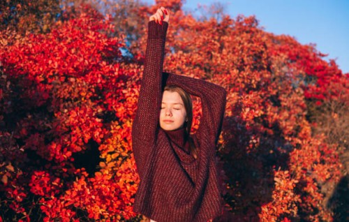 young woman in autumn forest in sunny day. trees with vibrant red and orange leaves. fall female portrait. knitted sweater and blue jeans. - fashion stock pictures, royalty-free photos & images