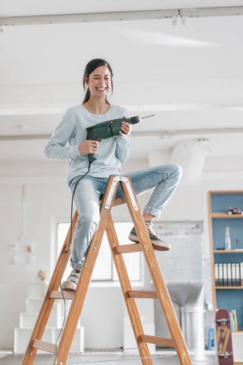 young woman in her new flat sitting on ladder, holding electric drill - home decoration stockfoto's en -beelden