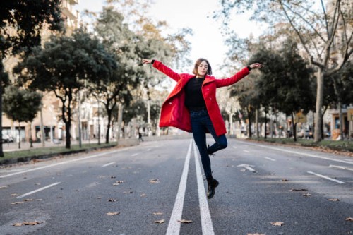 young woman in red jacket with arms raised dancing on street - fashion stock pictures, royalty-free photos & images