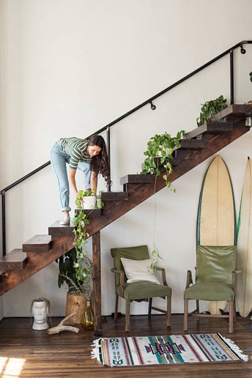 young woman on stairs in a loft caring for potted plant - home decoration stock pictures, royalty-free photos & images