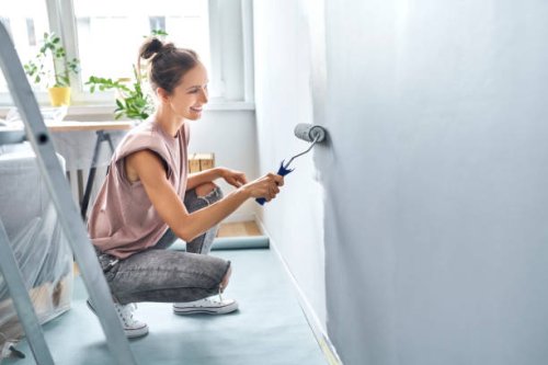 young woman painting wall with paint roller while crouching at home - home decoration stock pictures, royalty-free photos & images