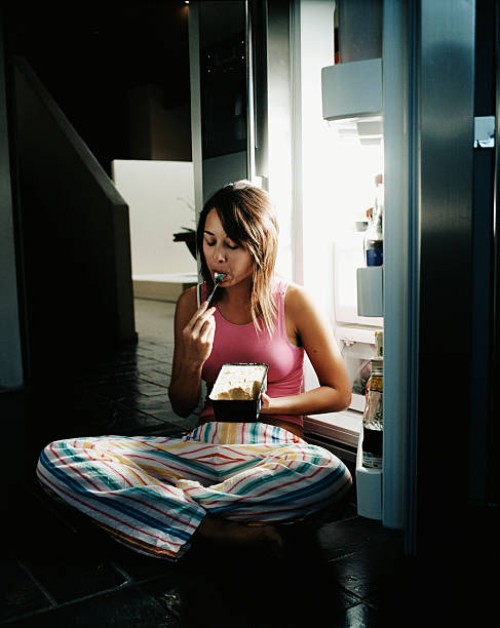 young woman sitting by open refrigerator, eating ice cream - junk food stock pictures, royalty-free photos & images